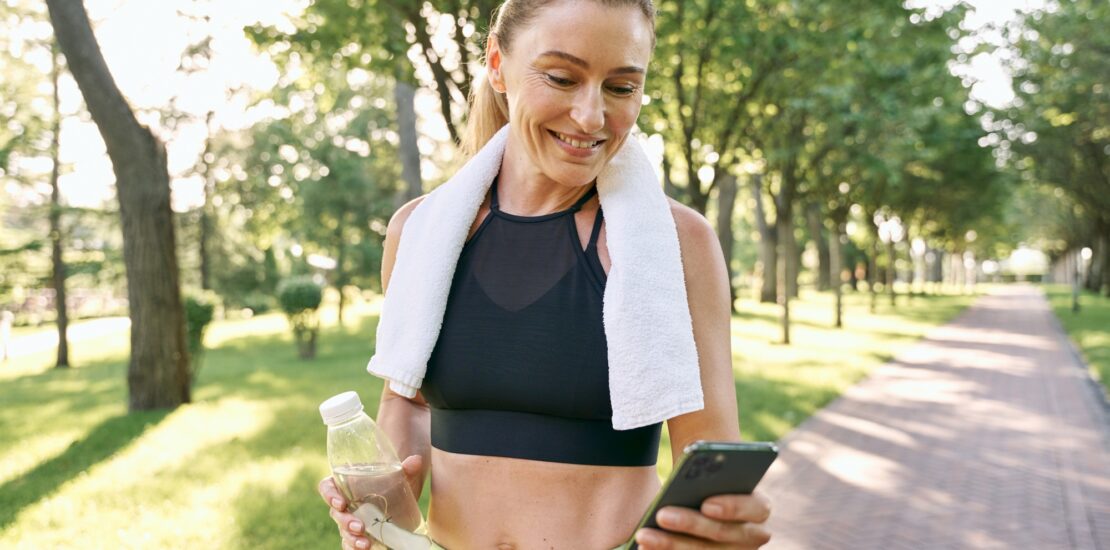 Energize your morning. Cheerful fit woman in sportswear refreshing, drinking water and using her