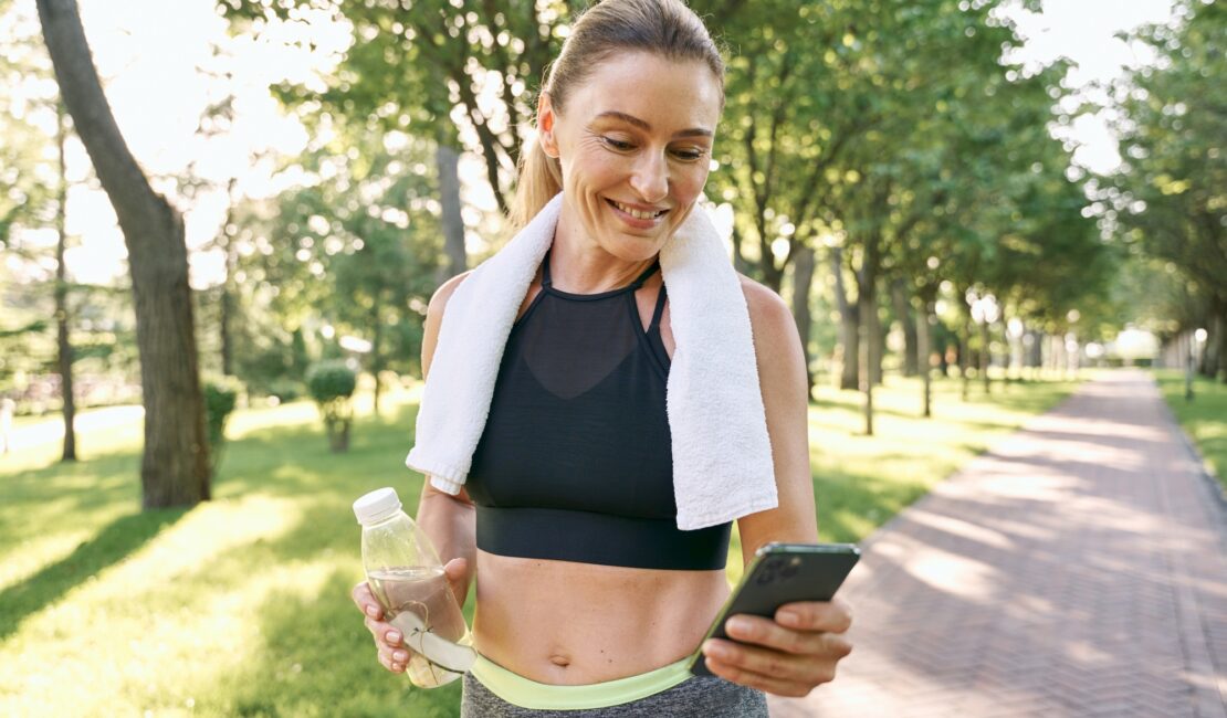 Energize your morning. Cheerful fit woman in sportswear refreshing, drinking water and using her