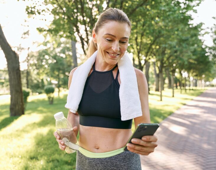 Energize your morning. Cheerful fit woman in sportswear refreshing, drinking water and using her