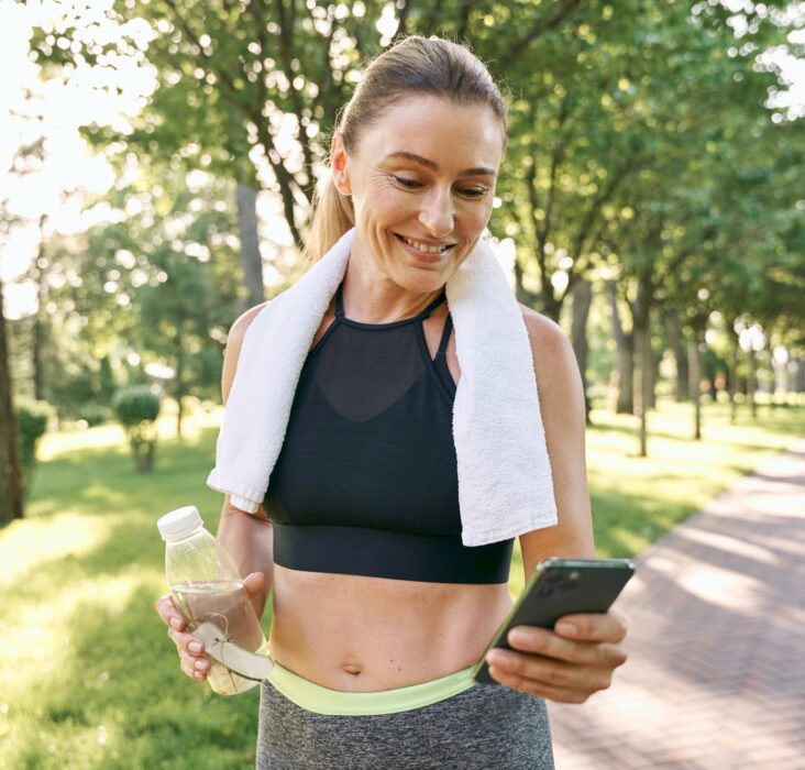 Energize your morning. Cheerful fit woman in sportswear refreshing, drinking water and using her