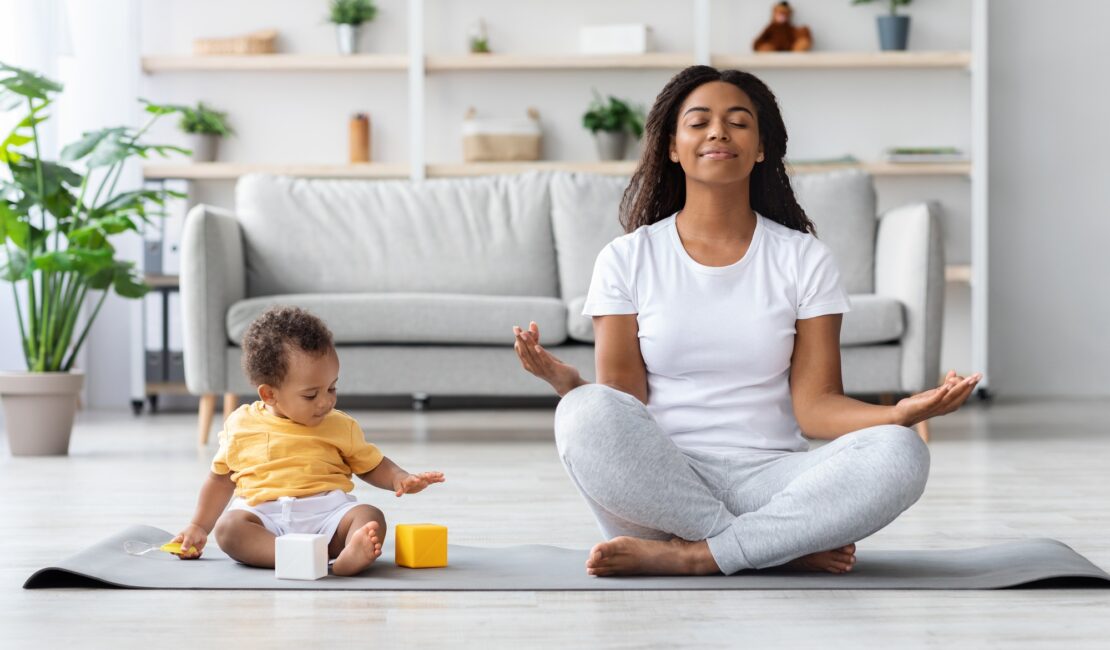 Mental Wellness Concept. Calm Happy Black Mother Meditating With Baby At Home