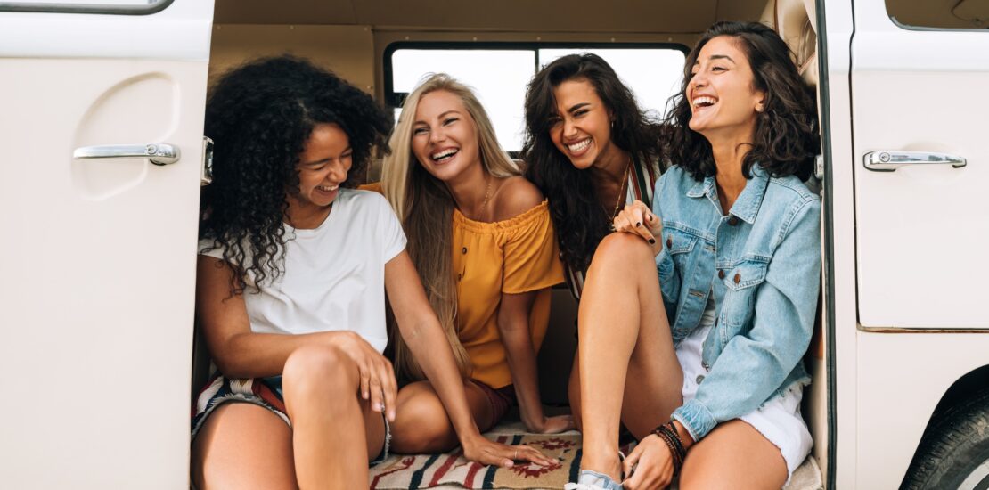 Multi ethnic group of women having fun while sitting in a car. Four friends traveling by car.