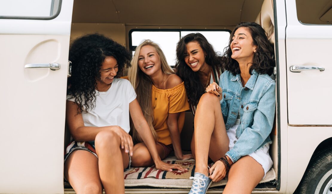 Multi ethnic group of women having fun while sitting in a car. Four friends traveling by car.
