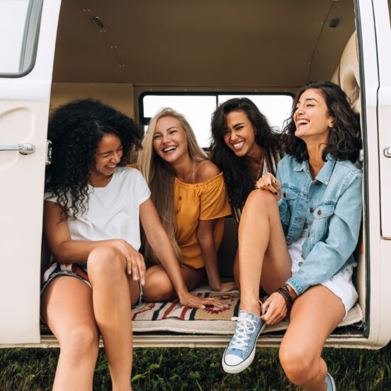 Multi ethnic group of women having fun while sitting in a car. Four friends traveling by car.