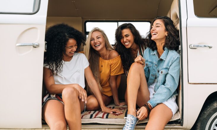 Multi ethnic group of women having fun while sitting in a car. Four friends traveling by car.