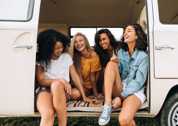 Multi ethnic group of women having fun while sitting in a car. Four friends traveling by car.