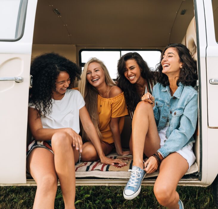 Multi ethnic group of women having fun while sitting in a car. Four friends traveling by car.