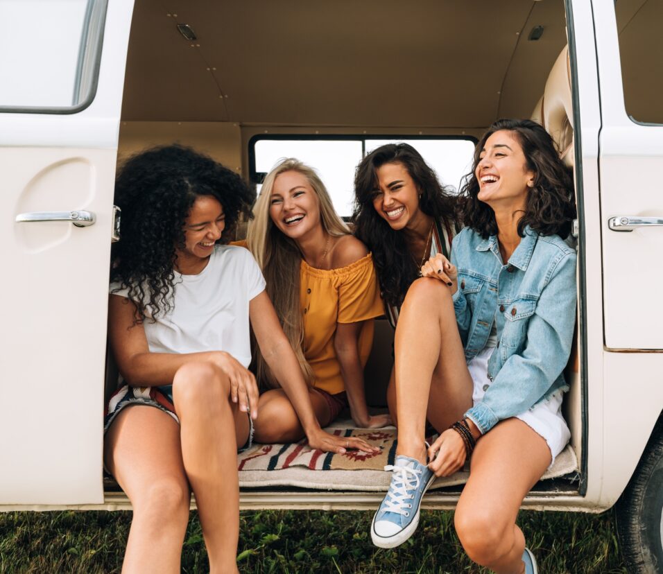 Multi ethnic group of women having fun while sitting in a car. Four friends traveling by car.
