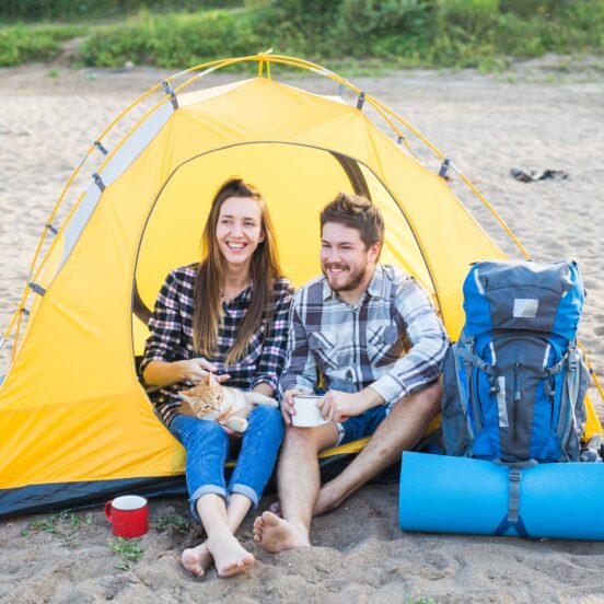 People, tourism and nature concept - Cute couple sitting with a cat in yellow tent