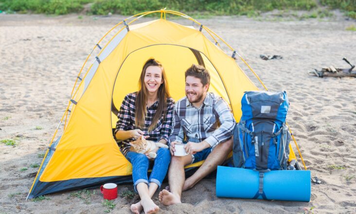 People, tourism and nature concept - Cute couple sitting with a cat in yellow tent