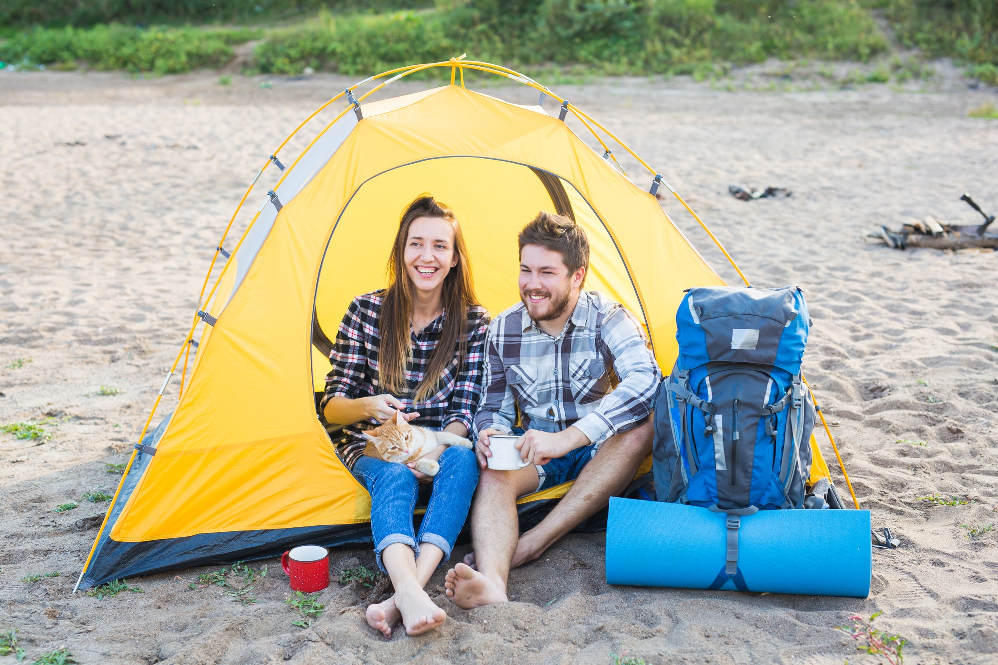 People, tourism and nature concept - Cute couple sitting with a cat in yellow tent
