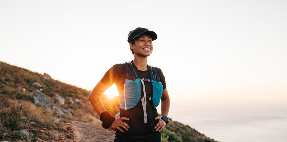 Portrait of sporty woman with cap relaxing at sunset. Female taking break on trail run.