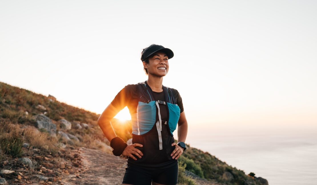 Portrait of sporty woman with cap relaxing at sunset. Female taking break on trail run.