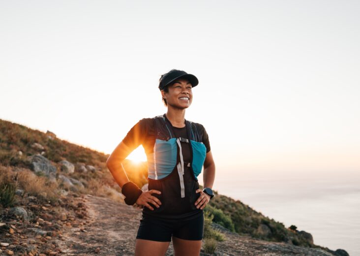 Portrait of sporty woman with cap relaxing at sunset. Female taking break on trail run.