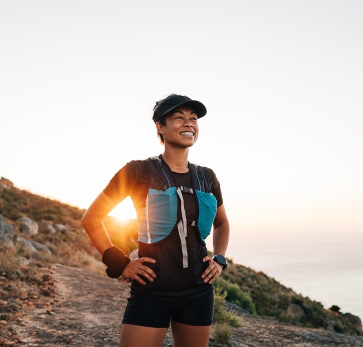 Portrait of sporty woman with cap relaxing at sunset. Female taking break on trail run.