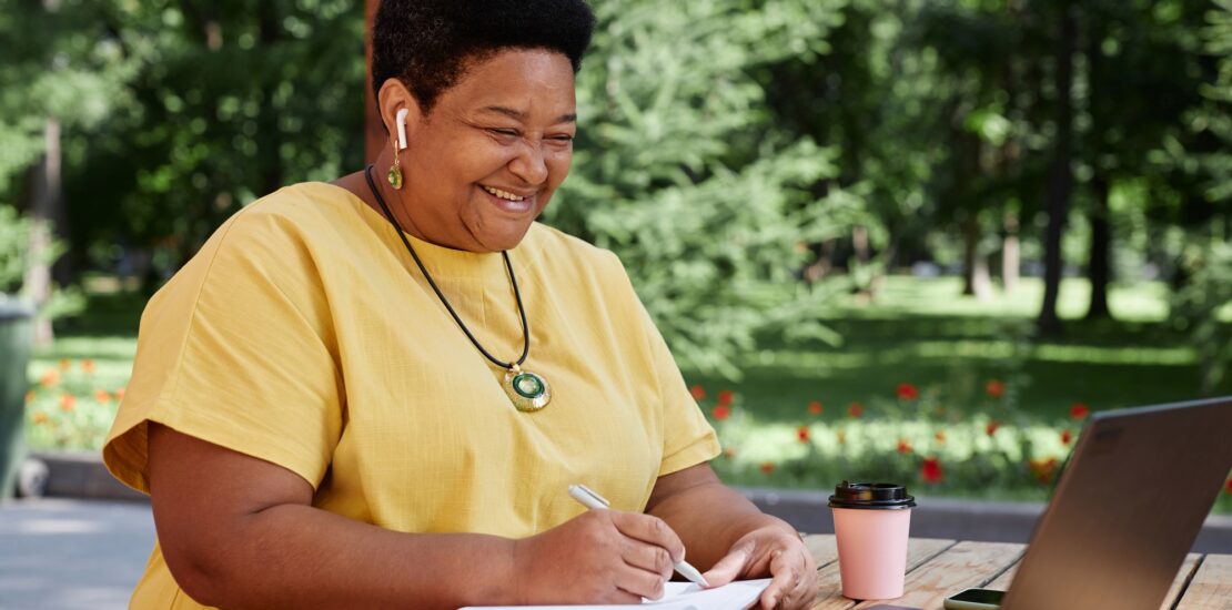 Smiling Black senior woman using laptop computer outdoors and using modern tech