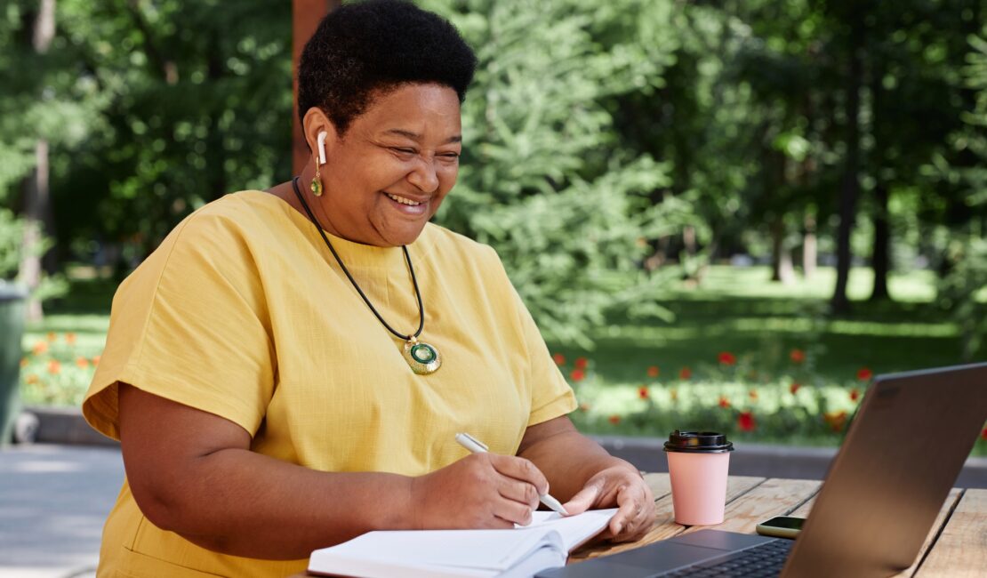 Smiling Black senior woman using laptop computer outdoors and using modern tech