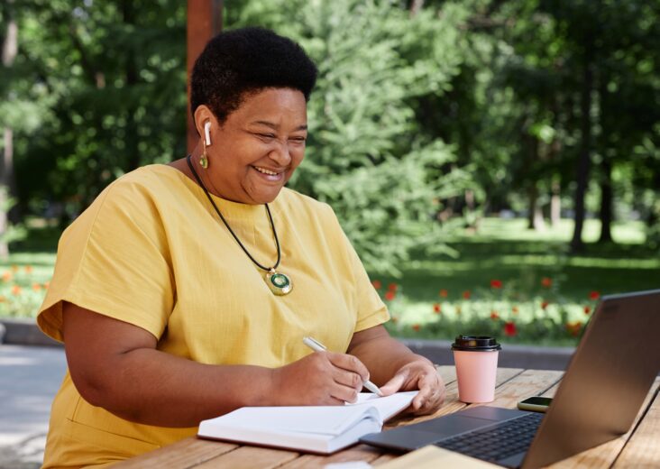 Smiling Black senior woman using laptop computer outdoors and using modern tech