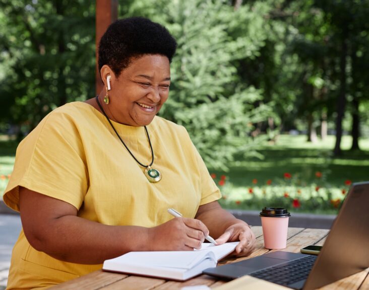 Smiling Black senior woman using laptop computer outdoors and using modern tech