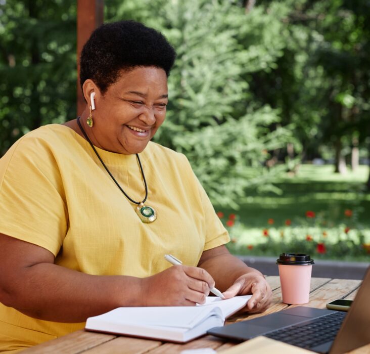 Smiling Black senior woman using laptop computer outdoors and using modern tech