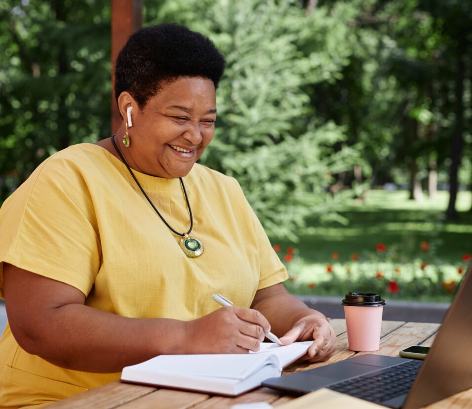 Smiling Black senior woman using laptop computer outdoors and using modern tech