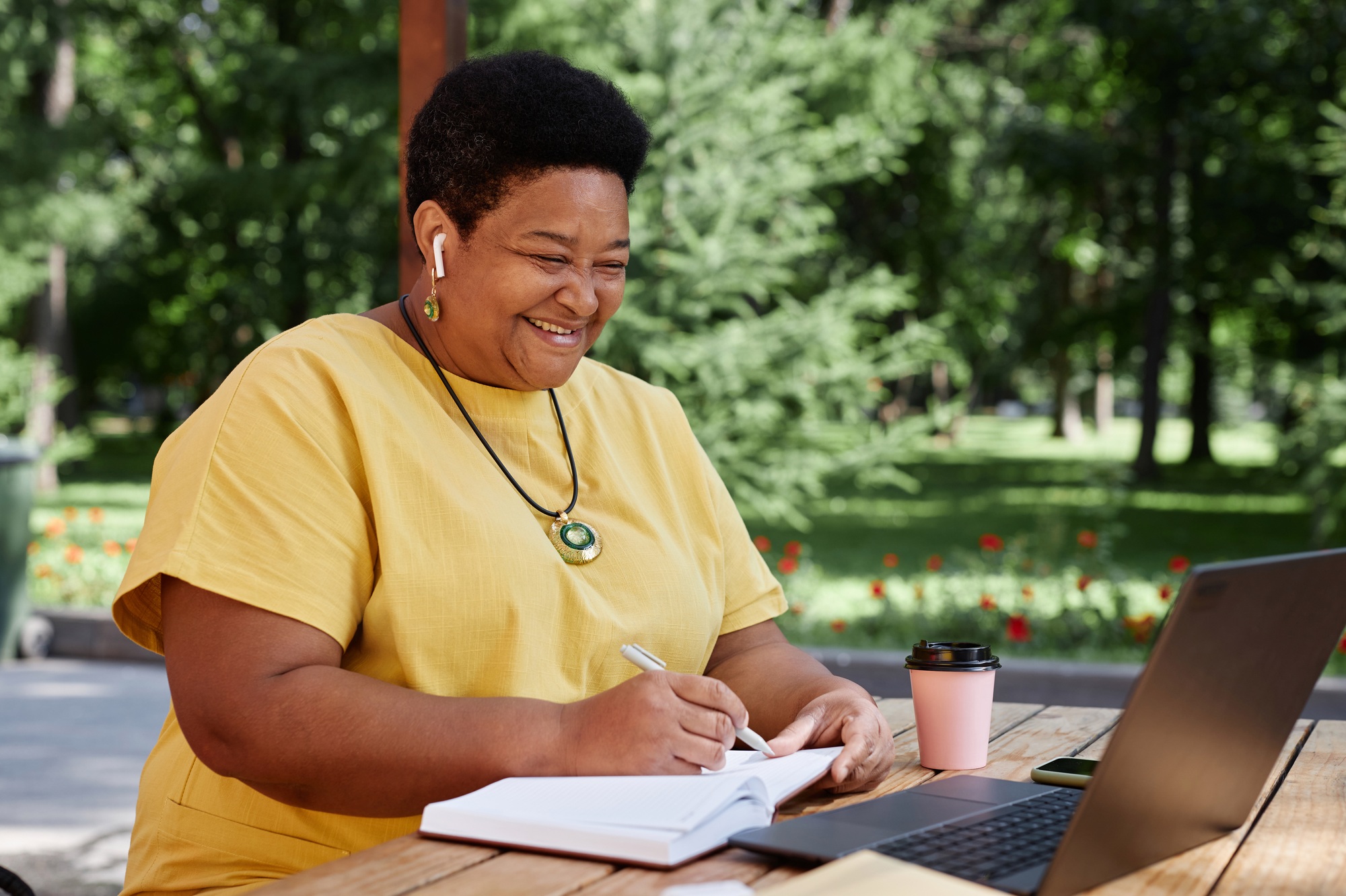 Smiling Black senior woman using laptop computer outdoors and using modern tech