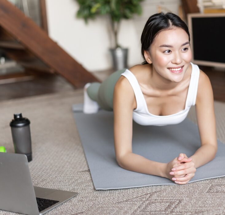 Sporty asian girl in activewear doing workout at home, follow video sport guide, online fitness