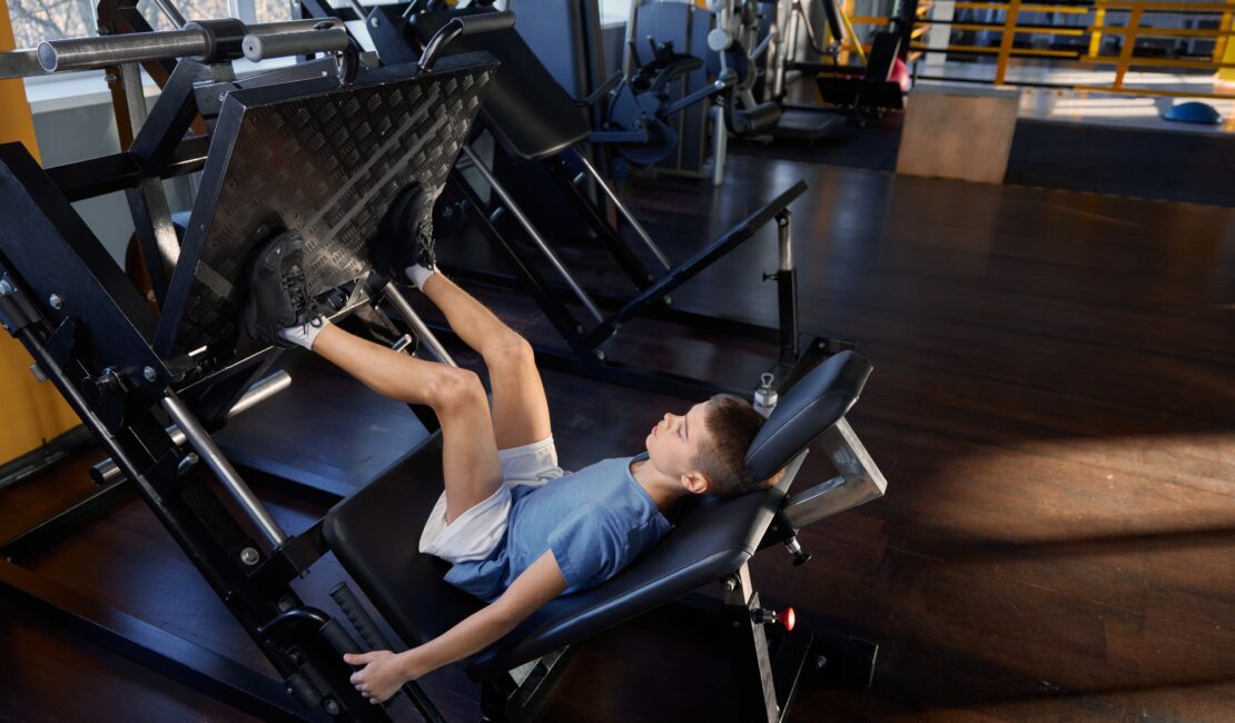 Teenage boy training legs at platform press strength machine
