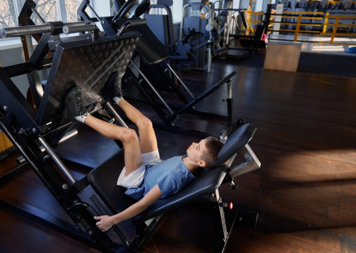 Teenage boy training legs at platform press strength machine