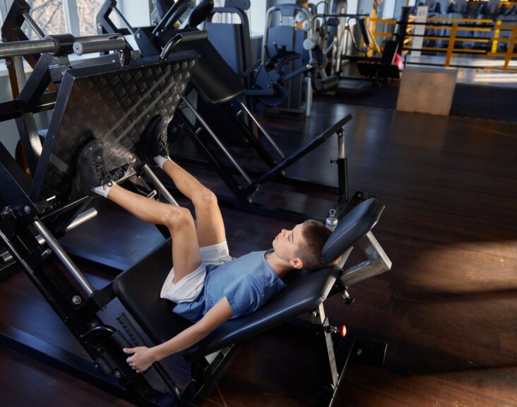 Teenage boy training legs at platform press strength machine