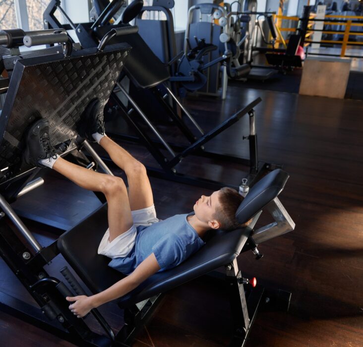 Teenage boy training legs at platform press strength machine