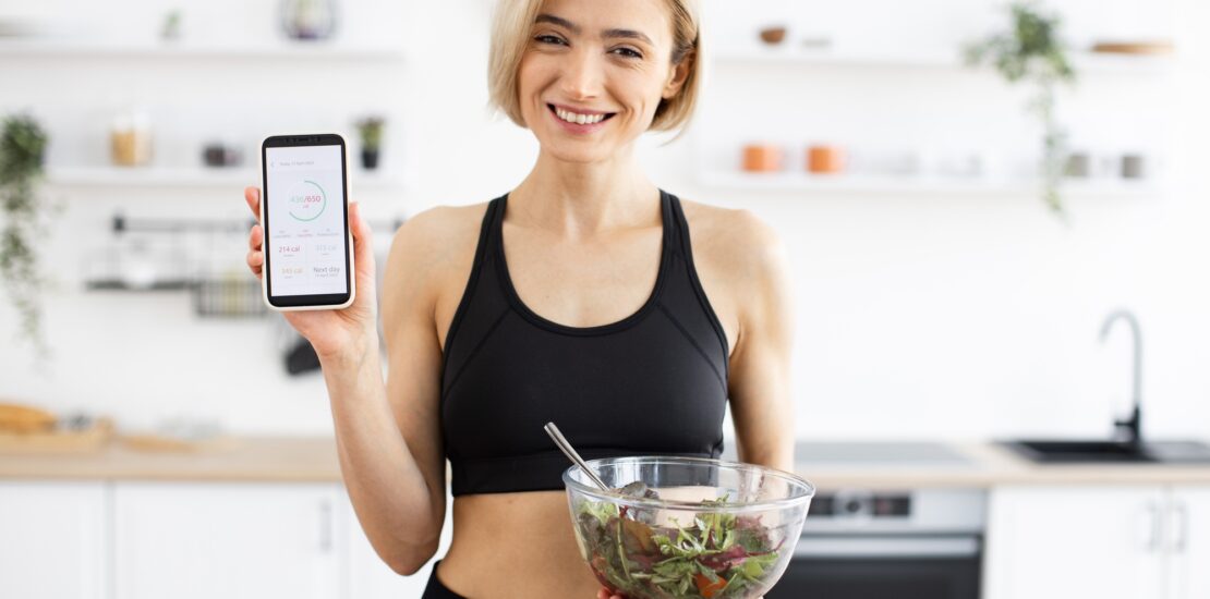 Woman in sportswear holding salad and displaying fitness app