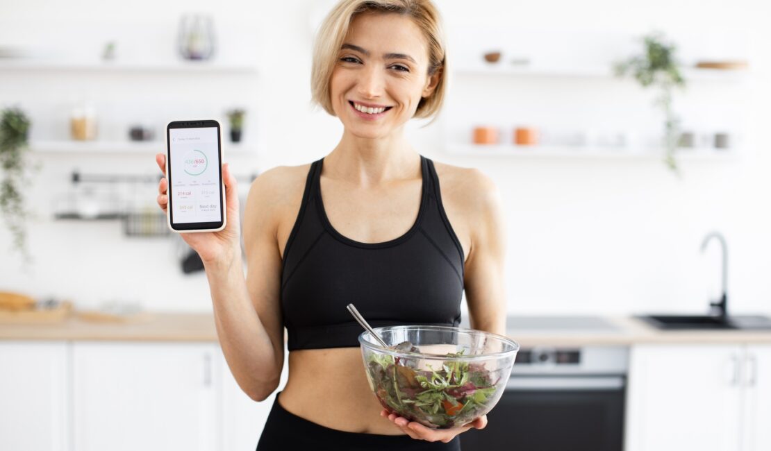 Woman in sportswear holding salad and displaying fitness app