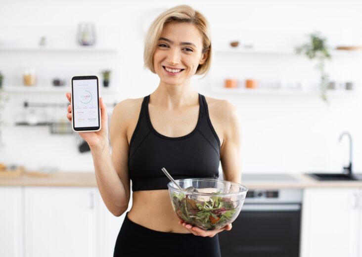 Woman in sportswear holding salad and displaying fitness app