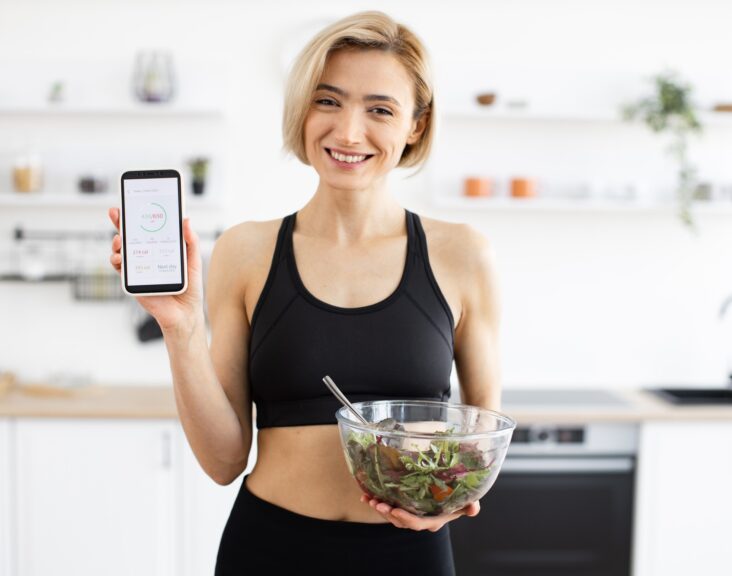 Woman in sportswear holding salad and displaying fitness app