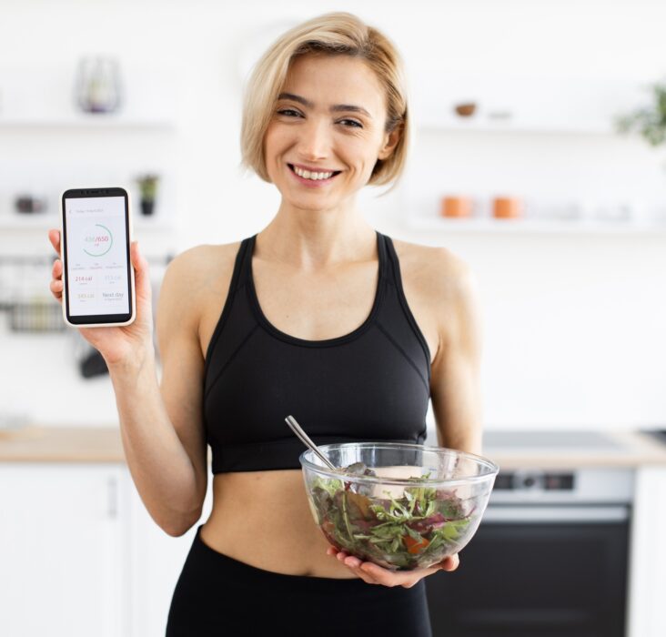 Woman in sportswear holding salad and displaying fitness app