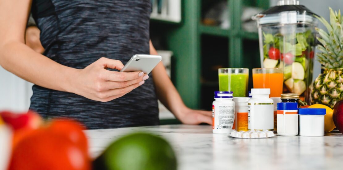 Young woman searching info about food supplements on her phone with fruits and additives