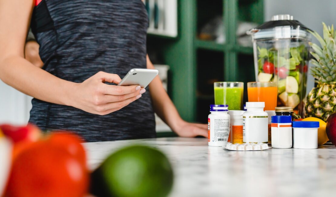 Young woman searching info about food supplements on her phone with fruits and additives