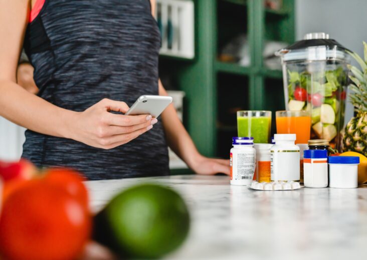 Young woman searching info about food supplements on her phone with fruits and additives