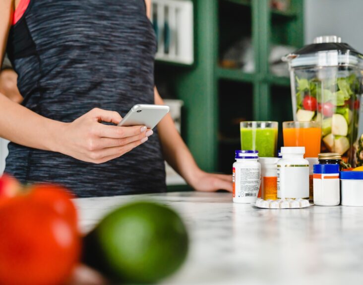 Young woman searching info about food supplements on her phone with fruits and additives