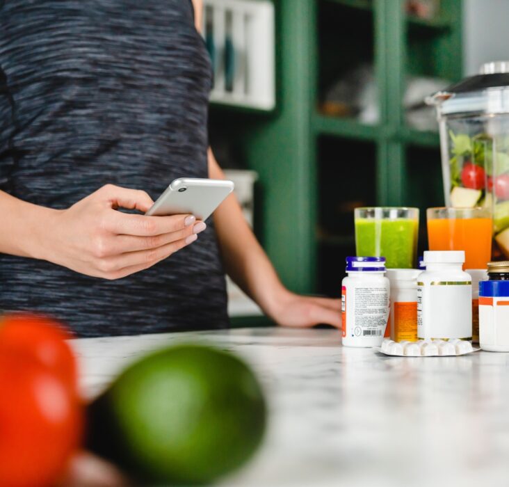 Young woman searching info about food supplements on her phone with fruits and additives